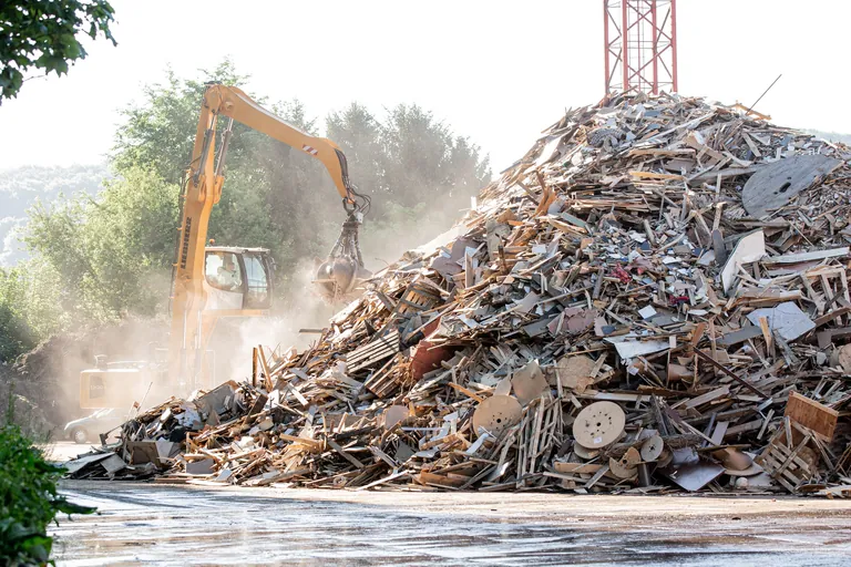 Ein Recyclinghof mit Bagger und großem Holzhaufen.