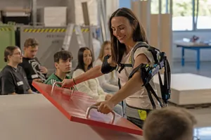 Eine junge Frau nutzt ein Exoskelett, um eine Platte anzuheben.