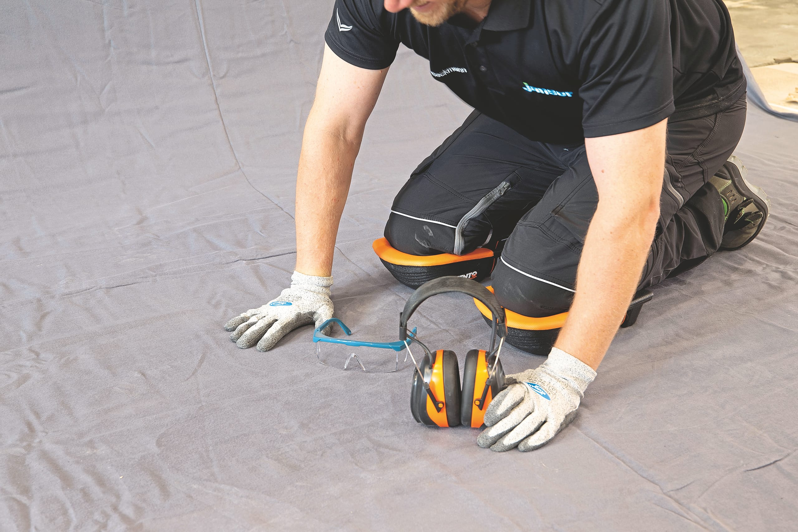 Handwerker kniet mit Sicherheitsausrüstung.